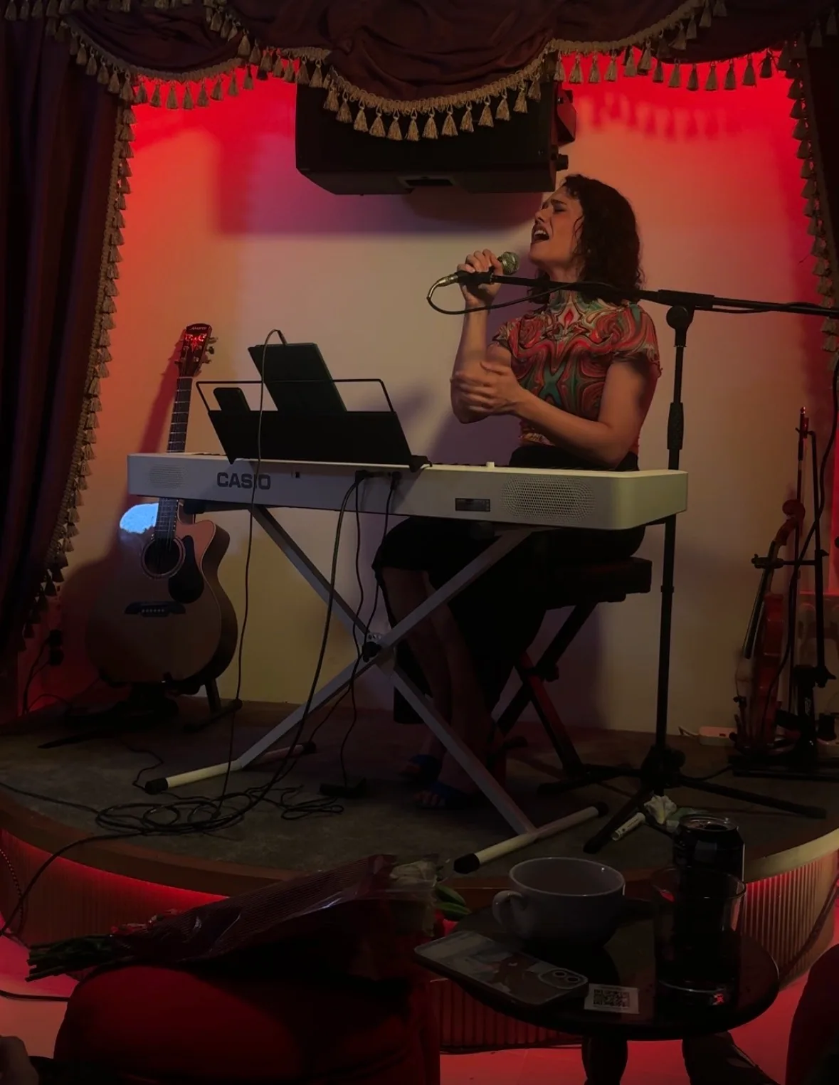 Melania Maggiore at the keyboard on the small stage in The Cave, with guitar and violin waiting beside her